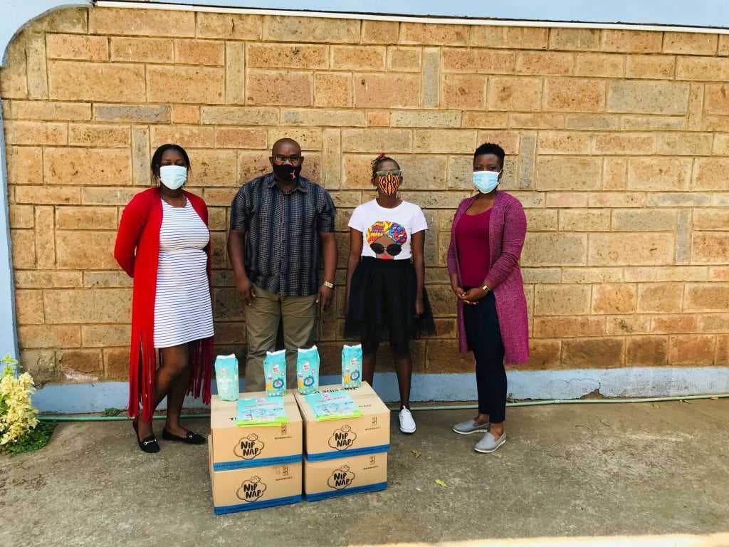 Four people in face masks standing behind boxes of donated diapers
